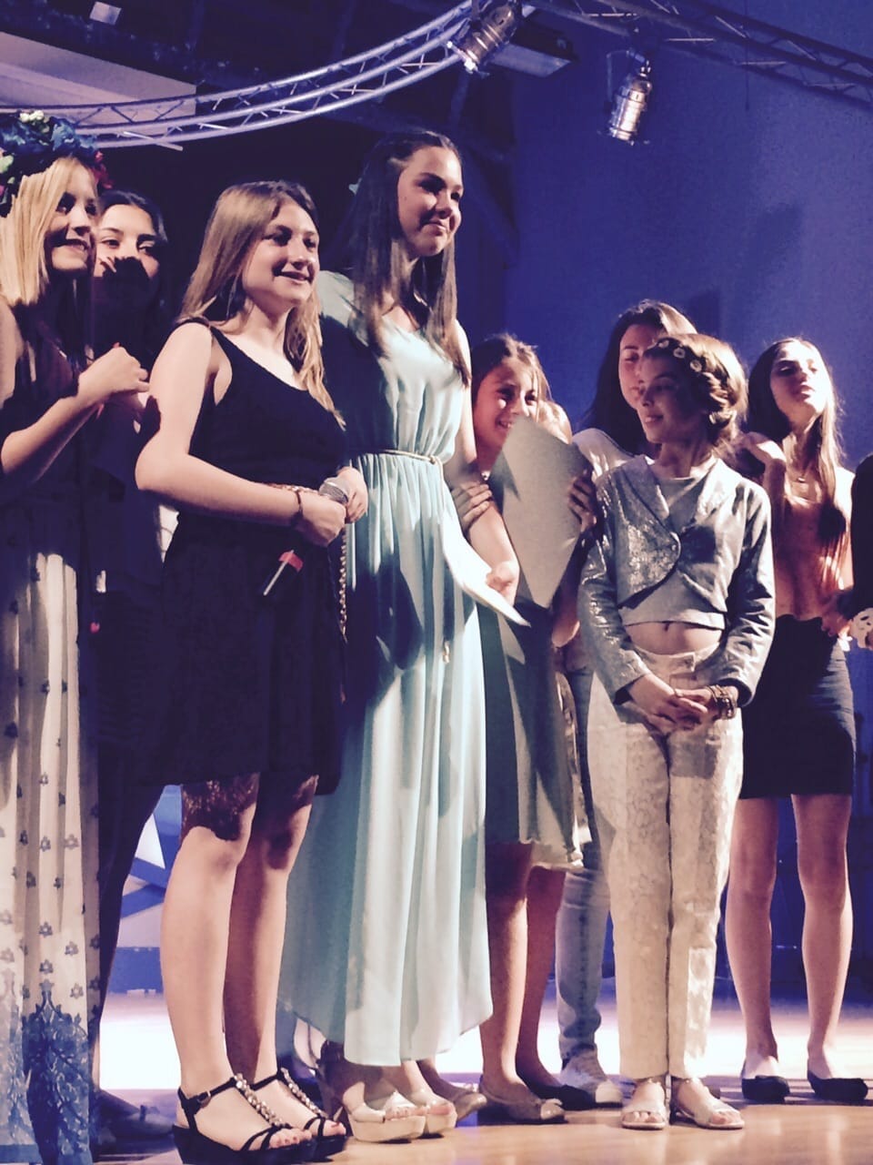 Rocío, adolescente y con vestido celeste, en el centro de un grupo de chicas sobre el escenario en una gala.